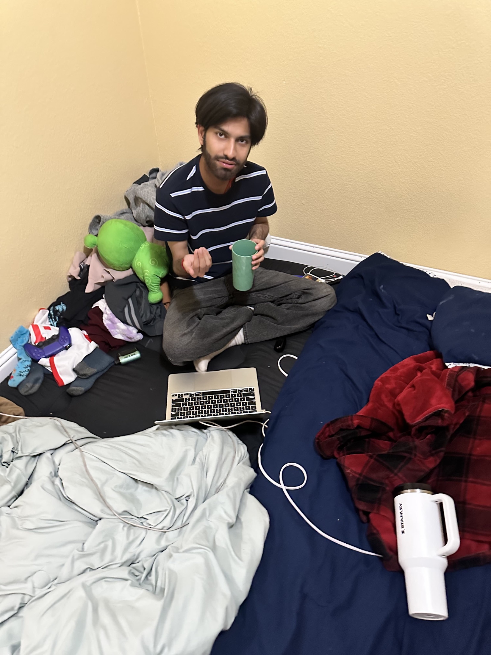 Kartikeya sitting on a bed with a cup and laptop nearby